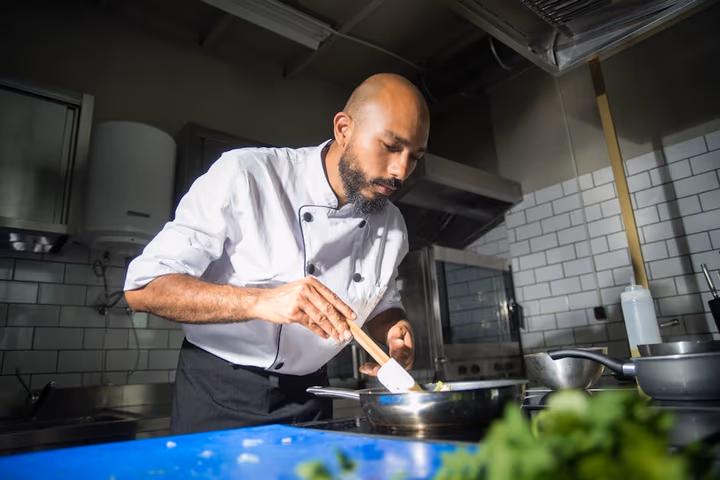 Chef préparant un plat en cuisine moderne, mettant en avant son expertise culinaire