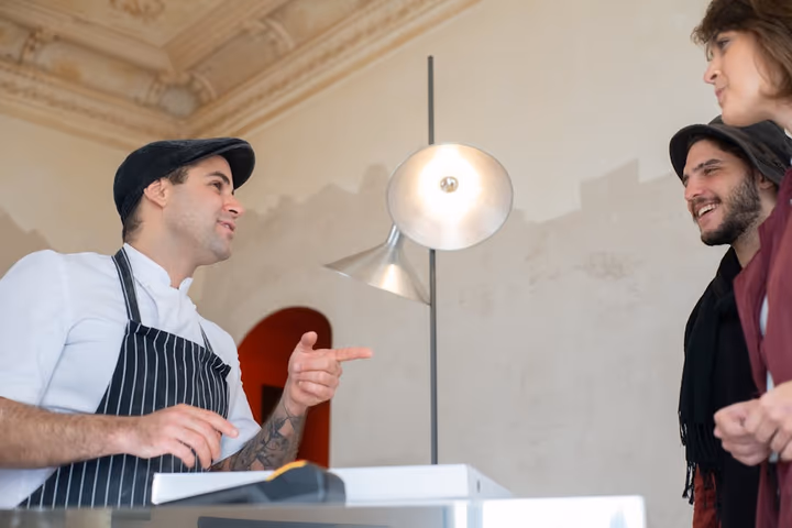 Chef souriant en conversation avec des clients satisfaits dans une ambiance chaleureuse de restaurant.